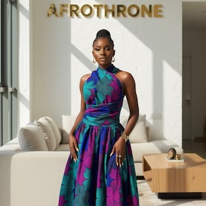 May include: A colourful, floor-length halter dress with a floral pattern in teal, purple, and blue. The dress has a fitted bodice and a full skirt. The word "AFROTHRONE" is displayed in gold lettering on the wall.