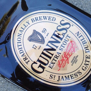 May include: A black glass bottle with a gold label that reads "Traditionally Brewed Guinness Extra Stout St. James's Gate Dublin". The label also includes the Guinness logo and the words "Imported Guinness Extra Stout".