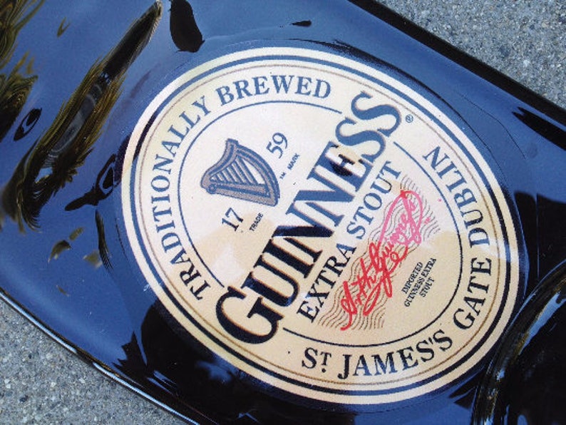 May include: A black glass bottle with a gold label that reads "Traditionally Brewed Guinness Extra Stout St. James's Gate Dublin". The label also includes the Guinness logo and the words "Imported Guinness Extra Stout".