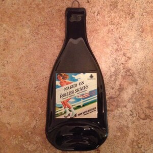 May include: Black glass bottle shaped like a wine bottle with a label that says "Naked on Roller Skates" and a picture of a woman on roller skates. The label also says "From South Australia".