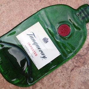 Op de afbeelding: Een groene glazen fles met een Tanqueray-label. Het label vermeldt "Ge&iuml;mporteerd" en "London Dry Gin". De fles heeft de vorm van een traditionele gin-fles en heeft een kurkstop.