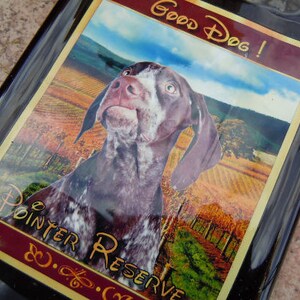 May include: A brown and white dog with a black nose and brown eyes. The dog is looking to the right. The dog is on a label with the text "Good Dog!" and "Pointer Reserve" in a brown and white font.