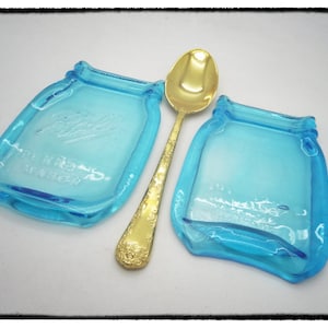 May include: Two blue glass jar-shaped spoon rests with a gold spoon in the center.