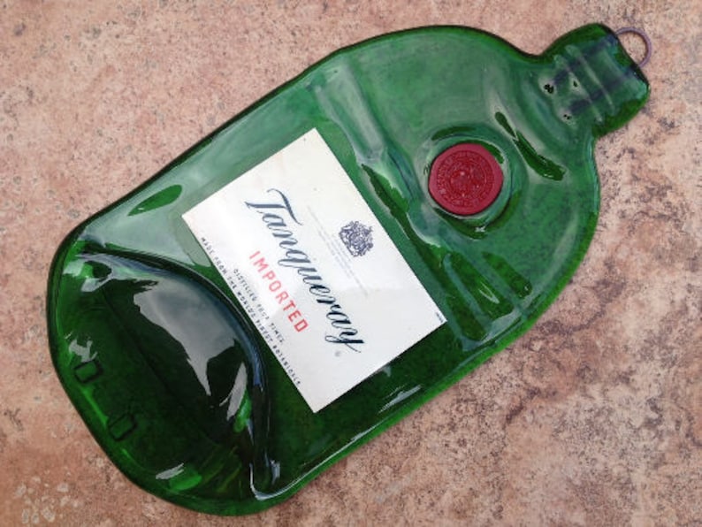 Pode incluir: Uma garrafa de vidro verde com um r&oacute;tulo que diz "Tanqueray Imported" e um selo de cera vermelho. A garrafa tem a forma de uma garrafa de gin tradicional e tem uma superf&iacute;cie texturizada.