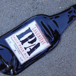 May include: A black glass bottle with a white label that reads "LAGUNITAS IPA INDIA PALE ALE Brewed and Bottled by the Lagunitas Brewing Co. Petaluma, California".