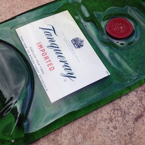 Op de afbeelding: Een groene glazen fles met een etiket waarop "Tanqueray Imported" en "Distilled four times - the world's finest botanicals" staat. De fles heeft een rode waszegel.
