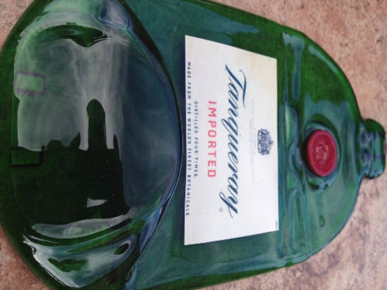 Op de afbeelding: Een groene glazen fles met een etiket waarop staat "Tanqueray Ge&iuml;mporteerd Viermaal Gedistilleerd Gemaakt van 's werelds beste botanicals". De fles heeft een rode dop en een doorzichtige glazen stop.