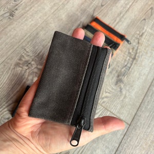 May include: A small gray zippered pouch with a black zipper. The pouch is made of a soft, textured fabric.