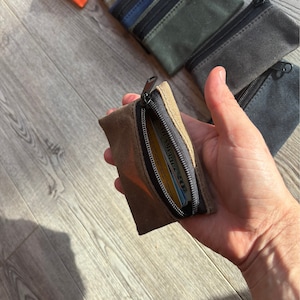 May include: A brown canvas zipper pouch with a black zipper. The pouch is open and a credit card is visible inside.