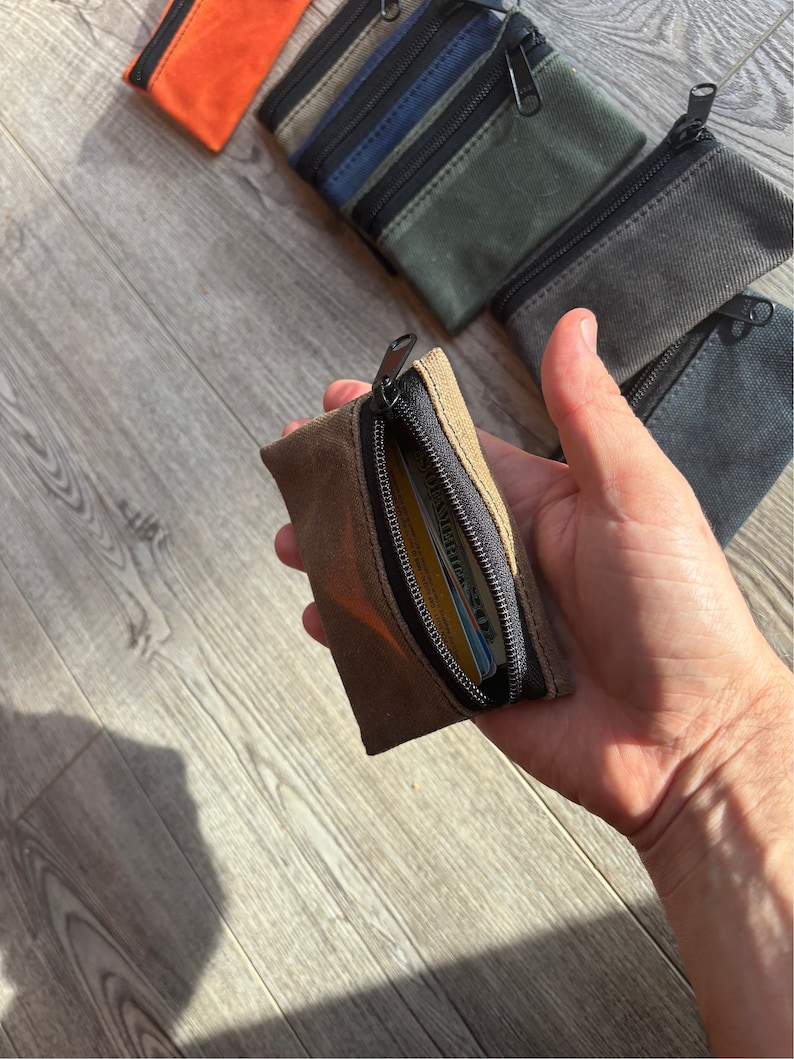 May include: A brown canvas zipper pouch with a black zipper. The pouch is open and a credit card is visible inside.