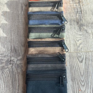 May include: A set of ten zippered pouches in various colors, including black, gray, brown, green, blue, and orange. The pouches are made of a canvas-like material and have two zippers.