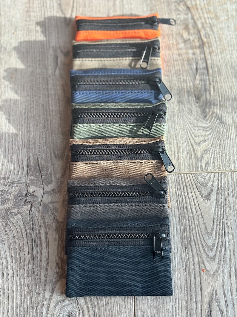 May include: A set of ten zippered pouches in various colors, including black, gray, brown, green, blue, and orange. The pouches are made of a canvas-like material and have two zippers.
