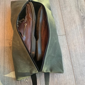 May include: A green canvas shoe bag with a zipper closure and a black strap. Two brown leather shoes are inside the bag.