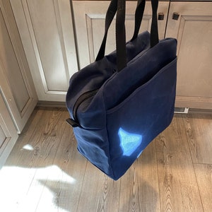 May include: A dark blue canvas tote bag with black handles. The bag has a zippered closure and a large pocket on the front.