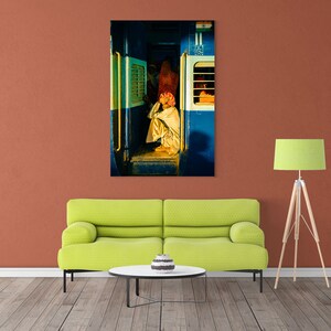 May include: A man sits on the floor of a train car, looking out the window. The train car is painted blue and white, and the window is open. The man is wearing a white shirt and a turban.