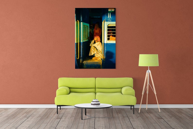 May include: A man sits on the floor of a train car, looking out the window. The train car is painted blue and white, and the window is open. The man is wearing a white shirt and a turban.