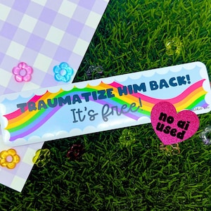 Puede incluir: Una pegatina con el texto "TRAUMATIZE HIM BACK! It's free!" sobre un diseño de arcoíris. También hay una pegatina rosa en forma de corazón con "no ai used". El fondo incluye un patrón de cuadros y césped artificial.