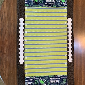May include: A green and blue fabric football field runner with the words "Seattle Seahawks" and numbers 10, 20, 30, 40, and 50 printed on the side.