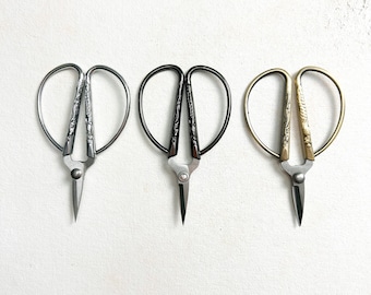 May include: Three pairs of decorative scissors with ornate handles. The scissors are silver, black, and gold.