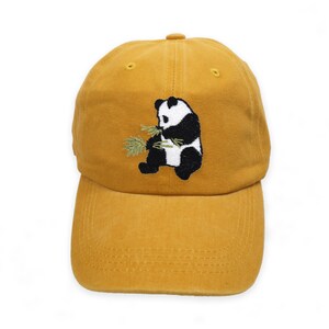May include: A mustard yellow baseball cap with an embroidered black and white panda eating bamboo.