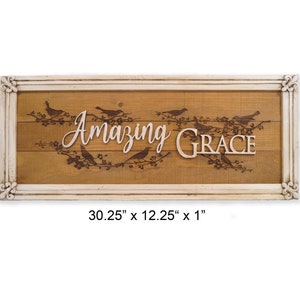 May include: A wooden sign with a white frame and the words "Amazing Grace" in a decorative font. The sign is decorated with a floral design and birds. The sign measures 30.25 inches by 12.25 inches by 1 inch.