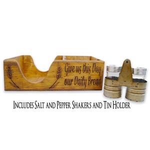May include: Wooden salt and pepper shaker holder with a napkin holder. The holder has the words "Give us this Day our Daily Bread" engraved on the front. It includes two metal salt and pepper shakers.