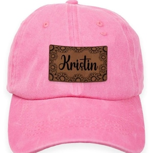 May include: Pink baseball cap with a brown leather patch that says "Kristin" in black cursive lettering.