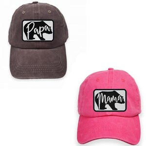May include: Two adjustable baseball caps, one brown and one pink, with a black bear silhouette and the words "Papa" and "Mama" in white lettering.
