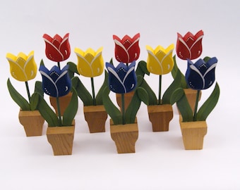 May include: A set of eight wooden tulip figurines, each painted in a different color: red, yellow, and blue. The tulips are in small wooden pots.