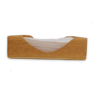 May include: A wooden napkin holder with a natural wood finish. The holder has a curved opening to hold napkins.