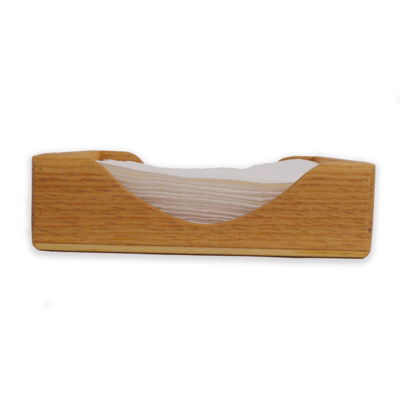 May include: A wooden napkin holder with a natural wood finish. The holder has a curved opening to hold napkins.