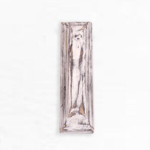 May include: A whitewashed wooden wall shelf with a distressed finish. The shelf has a rectangular shape with a raised edge around the perimeter.