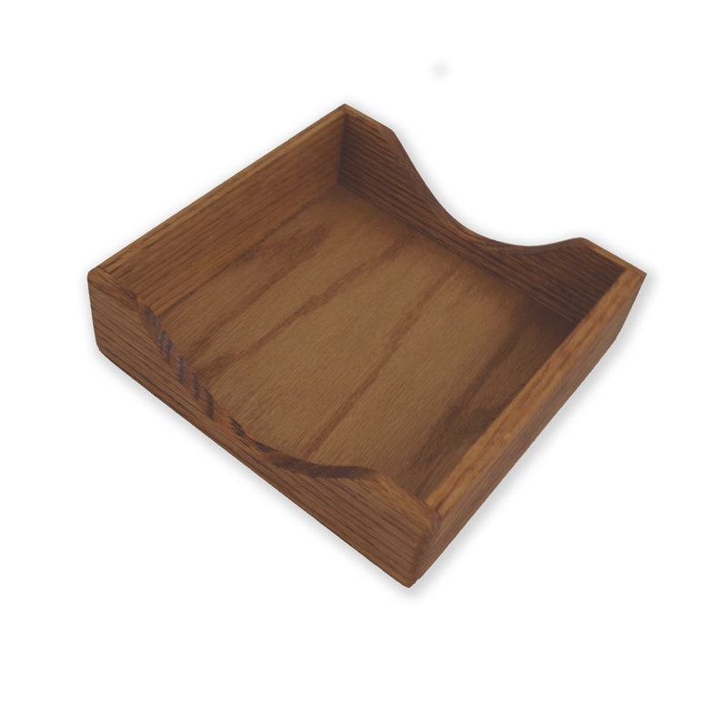 May include: A wooden square-shaped napkin holder with a curved interior. The holder is made of light brown wood with a natural wood grain.