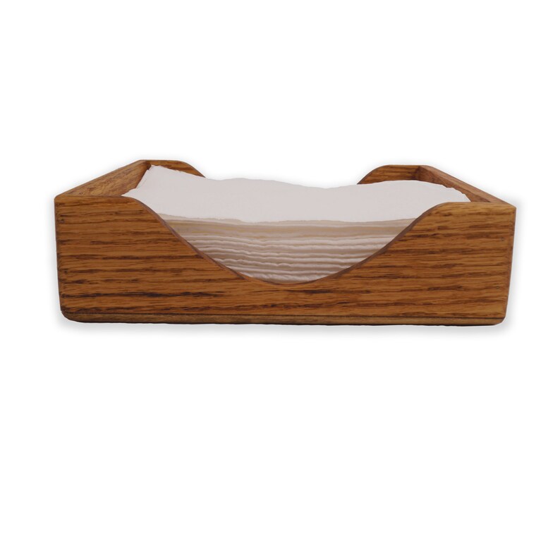 May include: A wooden napkin holder with a natural wood finish. The holder has a curved opening to hold napkins.
