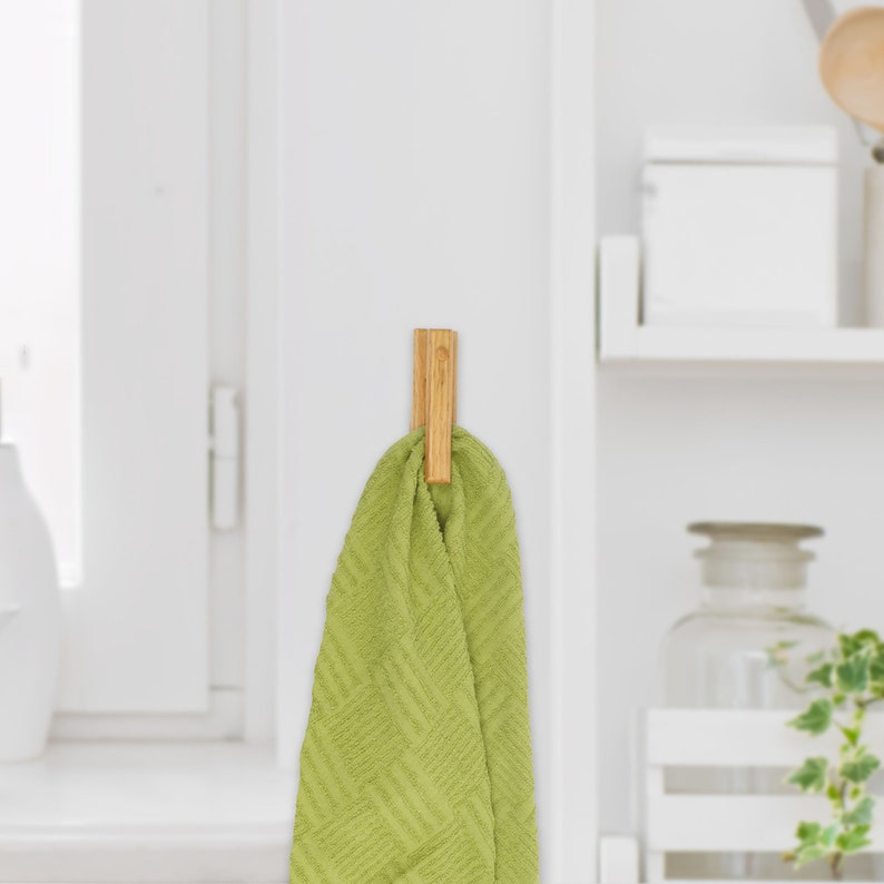 May include: A wooden hook with a green towel hanging from it. The hook is mounted on a white wall.