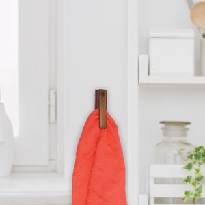 May include: A wooden towel hook with a red towel hanging from it. The hook is mounted on a white wall.