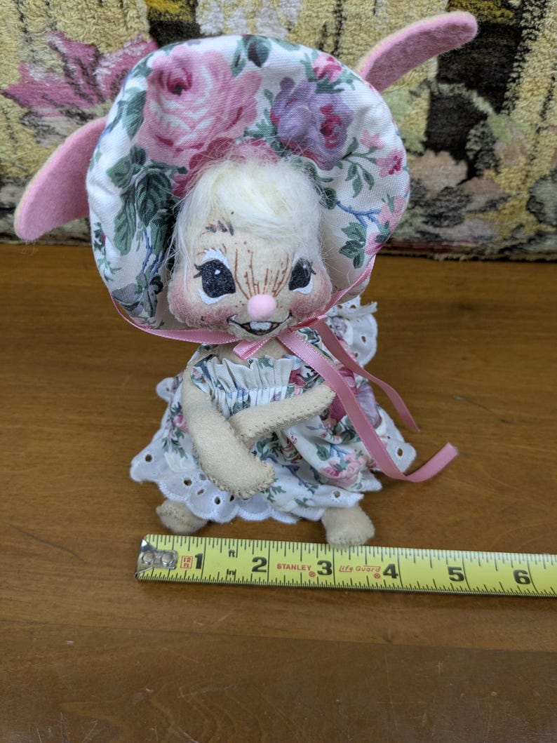 Puede incluir: Mu&ntilde;eca de conejito hecha a mano con un gorro y un vestido florales. La mu&ntilde;eca tiene una cara pintada con una nariz rosa y una peque&ntilde;a sonrisa. Las orejas de la mu&ntilde;eca son rosas y mide aproximadamente 7.6 cm de alto.