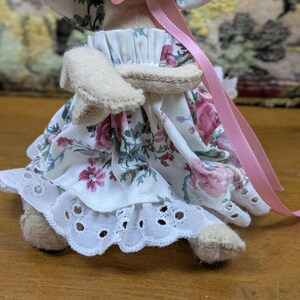 Puede incluir: Una mu&ntilde;eca hecha a mano con un vestido estampado floral con un ribete de encaje de ojal blanco. El vestido presenta rosas rosas y rojas. La mu&ntilde;eca tiene brazos y piernas beige, y una cinta rosa est&aacute; unida al sombrero de la mu&ntilde;eca.