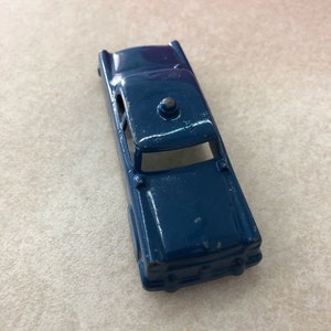 May include: A dark blue die-cast toy car featuring a sedan body style with a small circular light fixture mounted on the roof. The metal exterior shows signs of paint wear along the edges and roofline, with an open cabin and front hood detail.