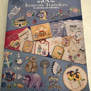 May include: A softcover book titled 2,002 Iron-on Transfers for painting and embroidery by Kooler Design Studio. The blue cover features a collage of various colorful iron-on designs including animals, flowers, food, and clothing items.