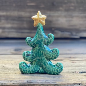 May include: A small ceramic Christmas tree ornament with a green glaze and a gold star on top.
