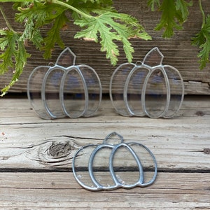 May include: Three clear glass pumpkin ornaments with silver-toned metal solder lines outlining the pumpkin shape. Each ornament features a small metal loop at the top for hanging. The pumpkins are transparent with a smooth, reflective surface.