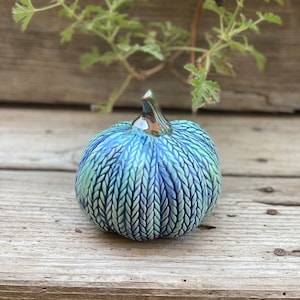 May include: A small blue and green ceramic pumpkin with a textured surface that resembles a knitted pattern.