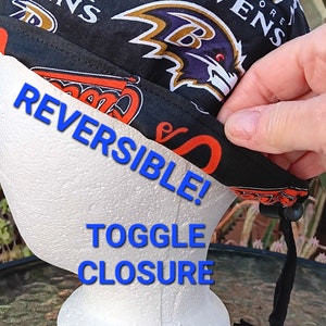 May include: Reversible black and purple baseball cap with the Baltimore Ravens logo. The cap has a toggle closure and is shown on a white mannequin head.