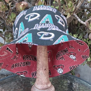 May include: A reversible bucket hat with a black and green patterned side featuring the text "Diamondbacks" and "Arizona" and a red side with the text "Arizona" and a baseball graphic.
