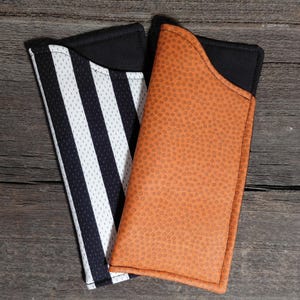 May include: Two rectangular fabric sleeves with black interior linings. One sleeve features a white and black vertical striped mesh pattern, while the other sleeve has a textured orange surface resembling the skin of a basketball.