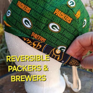May include: Reversible green and black fabric hat with the words "Packers" and "Brewers" printed on it. The hat has a tie string.