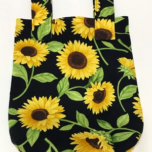 May include: A black fabric tote bag with a sunflower print. The bag has two straps and is made of a sturdy fabric.