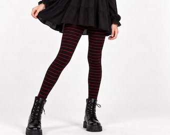 May include: Black leggings featuring thin horizontal red stripes, paired with a black long-sleeved dress and black lace-up combat boots with thick soles. The leggings have a fitted silhouette and the dress has a tiered skirt design.