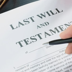 May include: A document titled "LAST WILL AND TESTAMENT" is being signed with a black pen. The document includes a space for a name and the text "resident of". The image also shows a pair of spectacles.